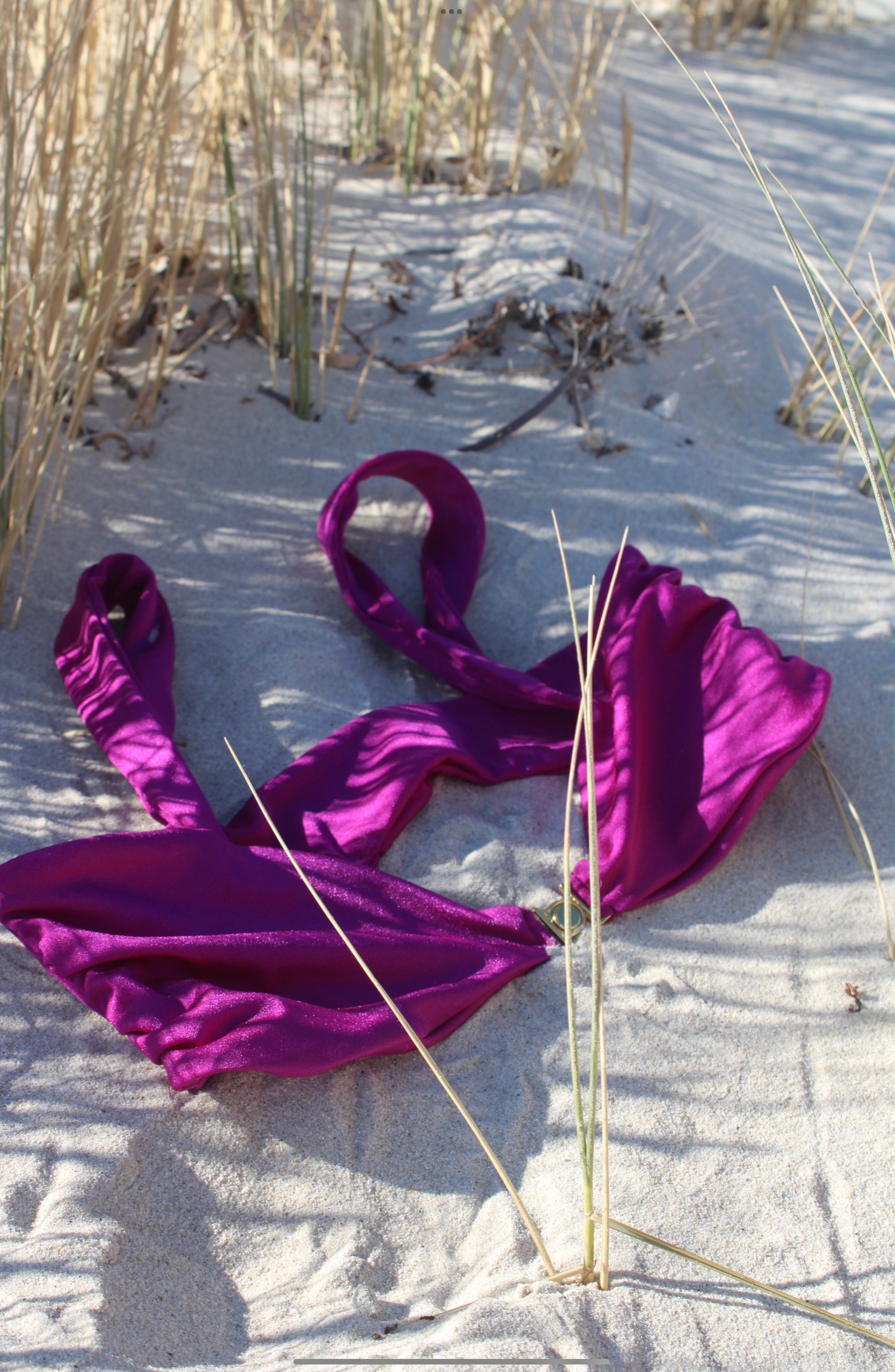 Purple bikini top lying on sandy beach.